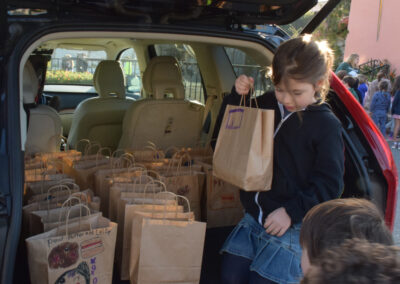 First graders load their lunch bags into a car for delivery.