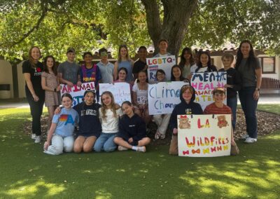 The 6th grade class poses under the oak tree with Mrs. Vaisman as they hold posters describing the causes they chose for activism.