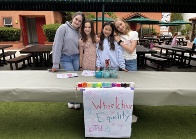 The 6th graders who chose People with Disabilities as their cause for activism pose in front of their booth prepared to make lanyards to decorate wheelchairs.