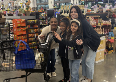 A group of moms and daughters pose with a shopping cart as they are about to begin their journey.