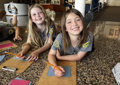 Two second-grade girls work on writing their notes of encouragement to be delivered with the food.