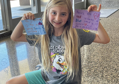 A second-grade girl holds up two notes she wrote to make the recipient feel special.